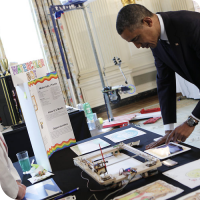 Sylvia instructs President Barack Obama as he draws the words "GO STEM!" on the iPad for the WaterColorBot to draw.