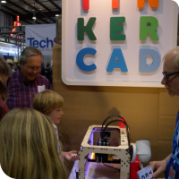 Sylvia standing in the foreground while a Makerbot Replicator prints Tinkercad models at the Tinkercad booth