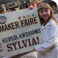 Sylvia holds a sign that says "Maker Faire Super Awesome Sylvia!"