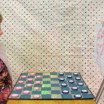 Sylvia sitting on the left of the checkers board, staring at a tripod