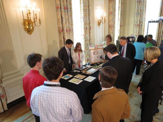 Sylvia showing Nate Ball, host of PBS Kids Design Squad, and a group of onlookers how her WaterColorBot works