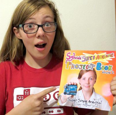 Sylvia pointing at a physical copy of her new book, "Sylvia's Super Awesome Project Book: Super-Simple Arduino"