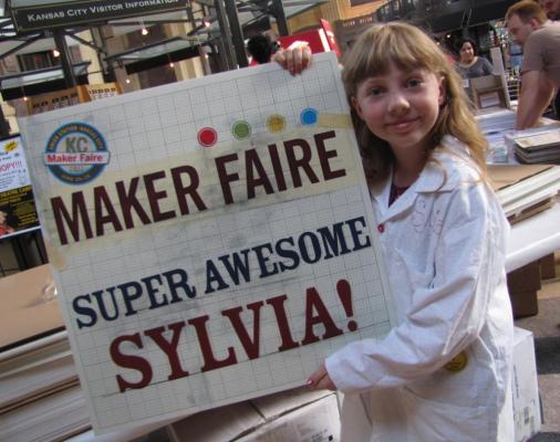 Sylvia holds a sign that says "Maker Faire Super Awesome Sylvia!"