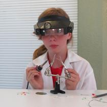 Sylvia wearing eye projection as she solders her pendant together.